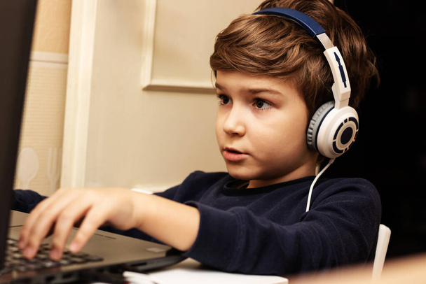 Small boy wearing headphones and using computer while playing video games at home. - Fotografie, Obrázek