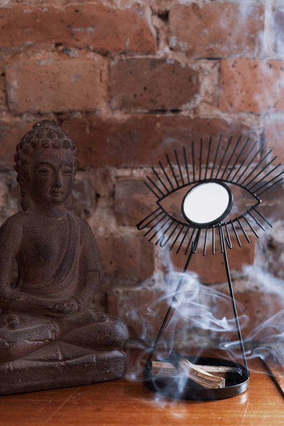 λεπτομέρεια διακόσμηση στο σαλόνι με κεραμικά αγαλματίδιο Buddha και palo santo μπαστούνια καύση με άρωμα καπνού. επούλωση, διαλογισμός, χαλάρωση - Φωτογραφία, εικόνα