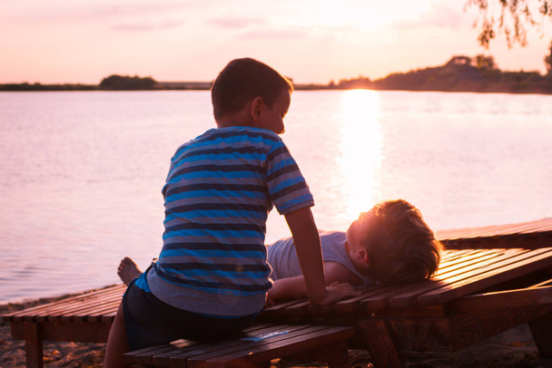 Two boys spending summer holiday at beach and relaxing on deck chairs at sunset. - Fotó, kép