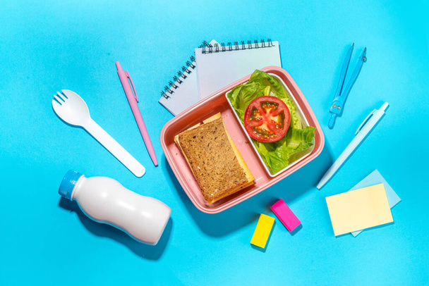 Healthy school meal, back to school concept. Children packed lunch box with balanced diet snack food - yogurt, cereal toast sandwich, apple, fresh vegetable salad, high-colored bright background - Photo, Image
