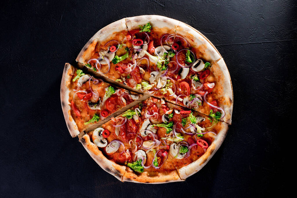 Vegan pizza with tomato sauce, cherry tomatoes, mushrooms, broccoli, red onion on black background. View from above. - Фото, изображение