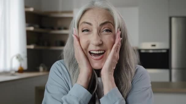 Delighted surprised mature middle-aged caucasian woman 60s lady looks amazed feel shock emotion win discounts triumph victory put hands on head. Elderly female retiree pensioner posing at home kitchen - Filmati, video