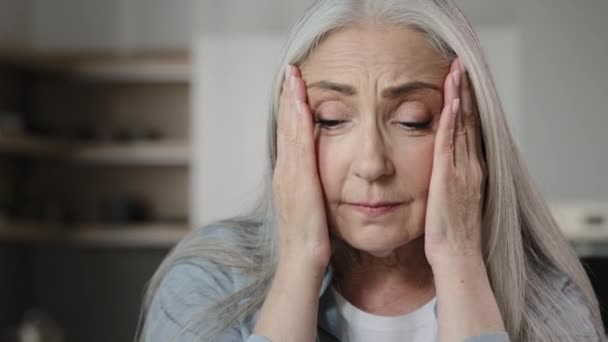 Sick old mature caucasian woman worried tired upset retiree grey-haired lady holding head massaging temples unbearable headache pressure suffering from migraine symptom panic attack feel pain at home - 映像、動画