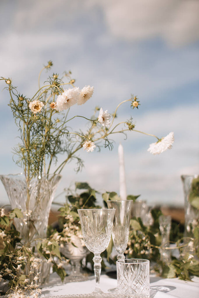 Decor for a wedding ceremony in a picturesque meadow. Wildflowers, crystal glasses, crystal plates, beautiful wedding tableware - Foto, imagen