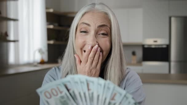 Happy female elderly winner old grey-haired mature woman caucasian lady of retirement age with pile of dollars pension money change currency win lottery cash prize monetary bonus surprised wow effect - Záběry, video