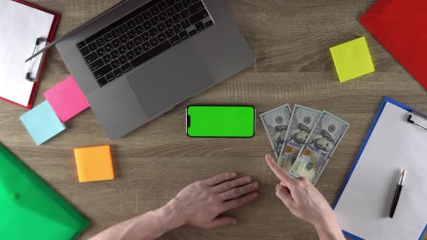 The coder is showing the programming courses on the phone green screen mockup concept. Horizontal position. 100 dollar bills on the table. - Filmagem, Vídeo