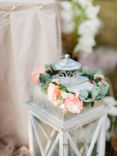 A wreath of pink and cream eustoma and eucalyptus leaves lies on a metal decorative lantern. - Fotó, kép