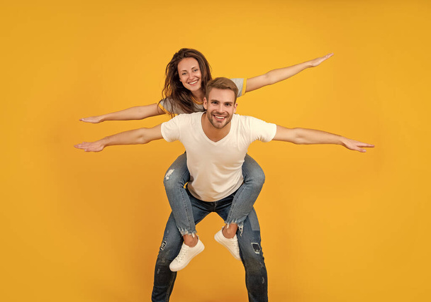 Happy playful woman and man pretend flying doing piggyback ride yellow background, fun. - Foto, imagen