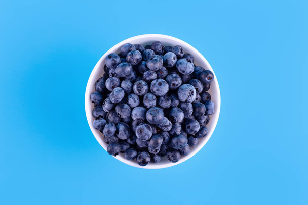 Fresh blueberries in white plate on blue background. Vegan and vegetarian concept. Summer healthy food. Flatla - Photo, image