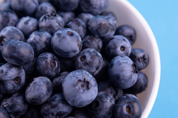 Blueberries on a macro scale. Dark berries in bowl close-up. Ripe blueberries isolated on blue background. Healthy, natural fruit - Foto, immagini