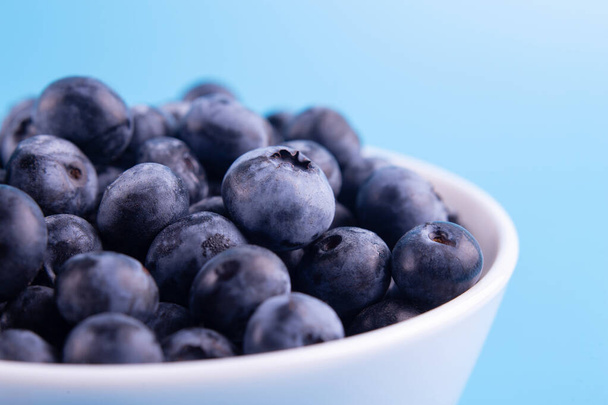 Blueberries on a macro scale. Dark berries in bowl close-up. Ripe blueberries isolated on blue background. Healthy, natural fruit - Foto, immagini