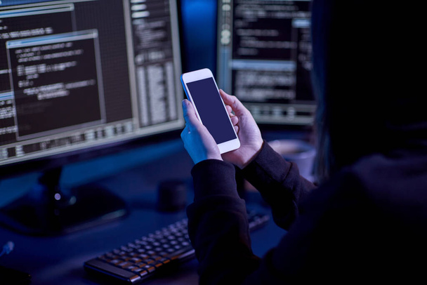 cybercrime, hacking and technology concept - close up of hacker with smartphone using computer virus program for cyber attack in dark room - Фото, зображення