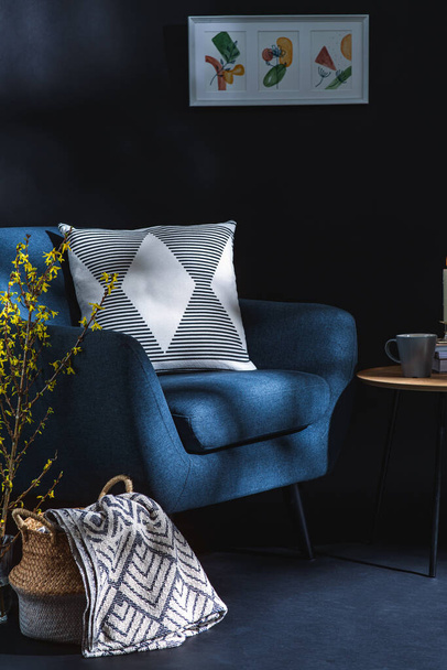 interior and home decor concept - close up της μπλε καρέκλας με μαξιλάρι, κουβέρτα σε ψάθινο καλάθι και κλαδιά δέντρων σε βάζο πάνω από μαύρο τοίχο - Φωτογραφία, εικόνα