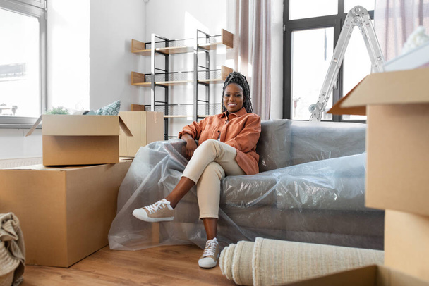 moving, people and real estate concept - happy smiling woman with boxes sitting on sofa at new home - Foto, imagen