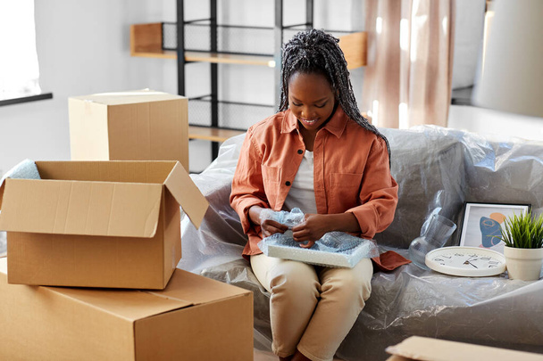 moving, people and real estate concept - happy smiling woman packing boxes sitting on sofa at home - 写真・画像