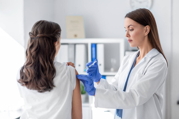 health, medicine and pandemic concept - female doctor or nurse wearing protective medical gloves with syringe vaccinating patient at hospital - Zdjęcie, obraz