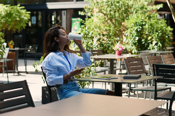 Mladá obchodní žena pití kávy a práci s tabletem v útulné pouliční kavárně. - Fotografie, Obrázek