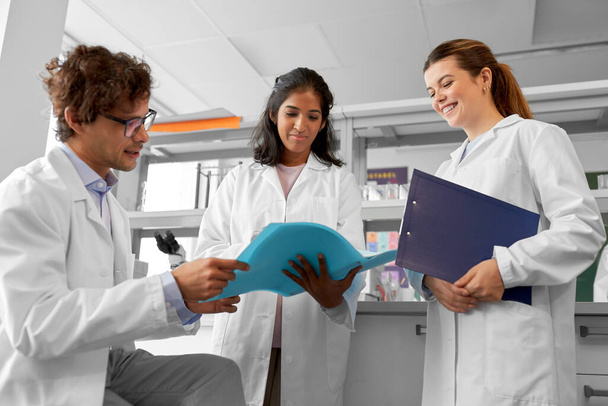 science research, work and people concept - international group of happy scientists with folder discussing report in laboratory - Fotoğraf, Görsel