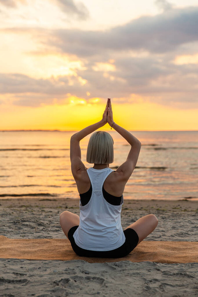 yoga, mindfulness and meditation concept - woman meditating in lotus pose on beach over sunset - Foto, Bild