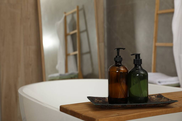 Wooden bath tray with bottles of shower gels on tub indoors, space for text - Fotoğraf, Görsel