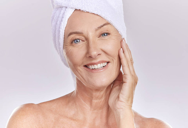 Portrait of happy woman wear a towel on head after enjoying a refreshing shower and healthy skincare. Senior beauty, cosmetic and face model smile while posing against a grey copy space background. - Photo, Image