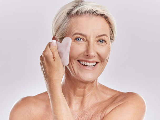 Skin care, hygiene and grooming by mature woman using a gua sha stone while giving herself a face massage. Happy senior female dace enjoying a beauty skincare routine to refresh and smooth wrinkles. - Foto, imagen
