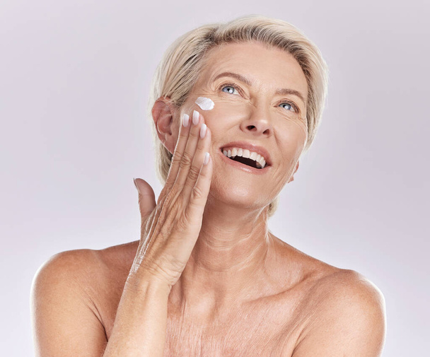 Woman with sunscreen on face for beauty skincare, showing cosmetics with smile and care for skin wellness standing on grey studio background. Content elderly model doing self care with cream. - Fotó, kép