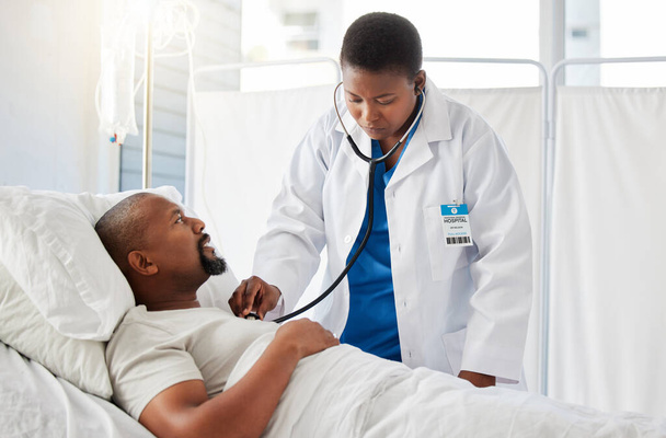 Medical doctor doing heart health checkup on patient in bed, listening for healthy heartbeat and consulting black man after surgery at hospital. Sick male person doing tests with healthcare worker. - Fotó, kép