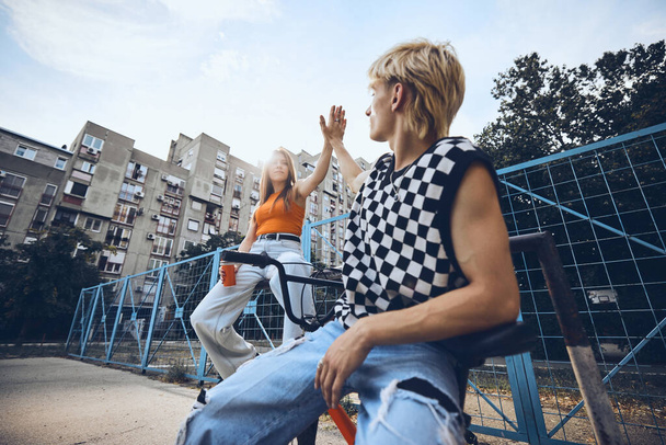 Tiener vrienden zitten in de stedelijke buitenkant en geven high five aan elkaar. - Foto, afbeelding