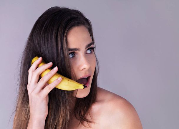 She cant believe her ears. Studio shot of an attractive young woman pretending to use a banana as a phone against a purple background - Фото, изображение