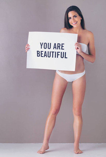 Just sending you a reminder to say...Studio portrait of an attractive young woman holding a sign that reads you are beautiful against a pink background - Foto, Bild