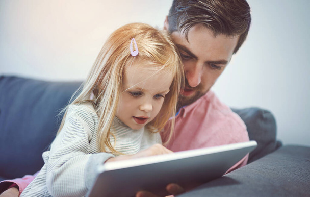 Bonding time in the age of the app. an adorable little girl using a digital tablet with her father on the sofa at home - Fotoğraf, Görsel