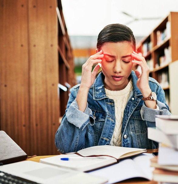 The student life is filled with plenty of headaches. a university student looking stressed out while working in the library at campus - Fotoğraf, Görsel
