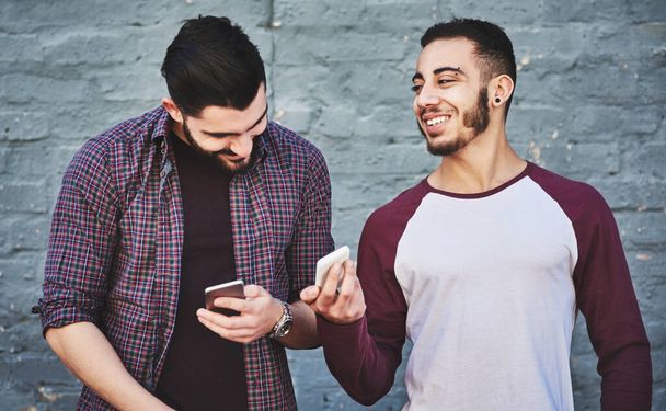 Bro, look who wants to chat. two young men standing outdoors and using a mobile phone against a gray wall - Fotografie, Obrázek
