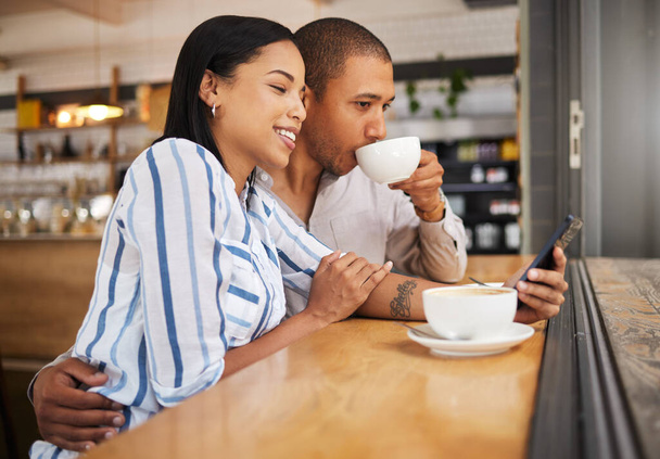 Couple using social media on a phone and drinking tea in a coffee shop together. Happy man and woman with 5g mobile smartphone texting and searching on an online app and enjoy a date at a cafe. - 写真・画像