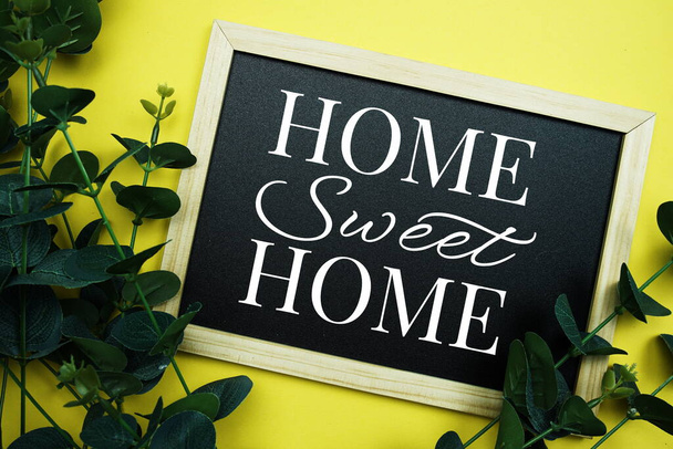Home Sweet Home typography text written on wooden blackboard with green eucalyptus decoration on yellow background - Photo, image