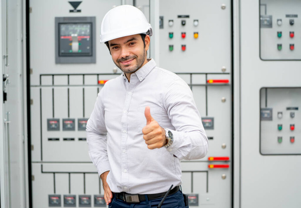 Engineer man stand in front of electrical control panel and show thumbs up to camera with smiling during work in construction site. - Foto, Bild