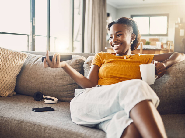 Relaxed, carefree and smiling young female watching tv and streaming movie at home on her living room sofa. Happy, casual and comfortable woman sitting on her couch and enjoying her leisure free time. - 写真・画像