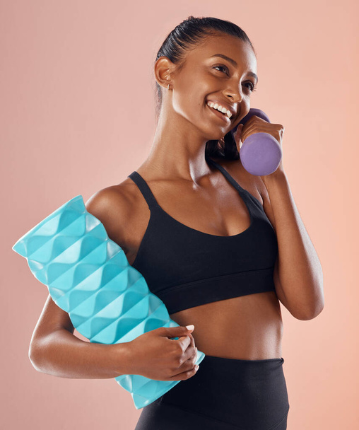 Fitness, active and healthy woman holding a dumbell, foam roller and smile after sports training against studio background. Happy fit lady feel slim, happy and cheerful after gym, workout or exercise. - 写真・画像