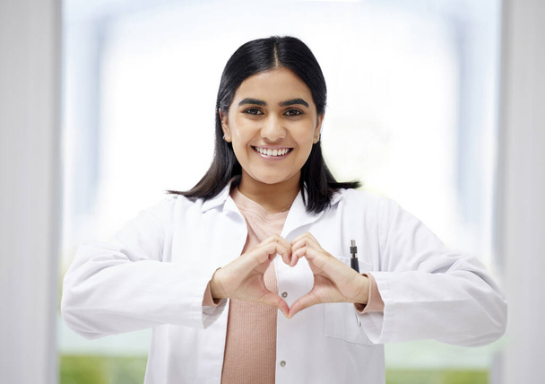 Smiling, caring medical doctor with heart sign hands gesture in modern clinic or hospital. Happy, positive and wellness young healthcare worker or physician with support and care symbol. - Foto, imagen
