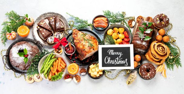 Delicious Christmas themed dinner table with roasted meat, potato, appetizers and desserts. Holiday concept. Top view on a grey background. Holiday concept. - Foto, afbeelding