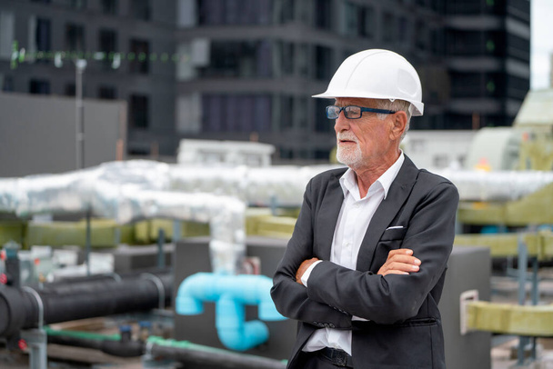 Senior engineer man stand with arms crossed and look to his right side also stand on rooftop of construction site. - 写真・画像
