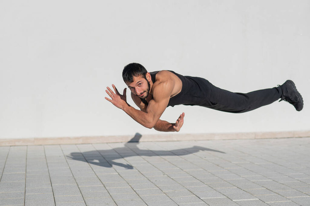 A man in black sportswear jumps while doing push-ups outdoors - Foto, afbeelding
