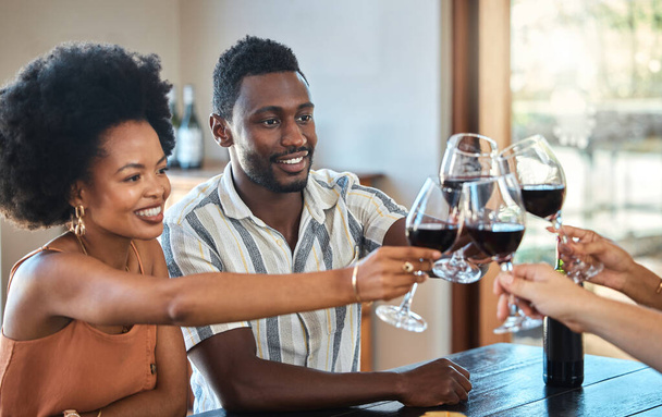 Black couple celebrating their anniversary with friends, toasting and drinking red wine. Happy girlfriend and boyfriend bonding at a family gathering, together for an engagement or proposal. - Zdjęcie, obraz