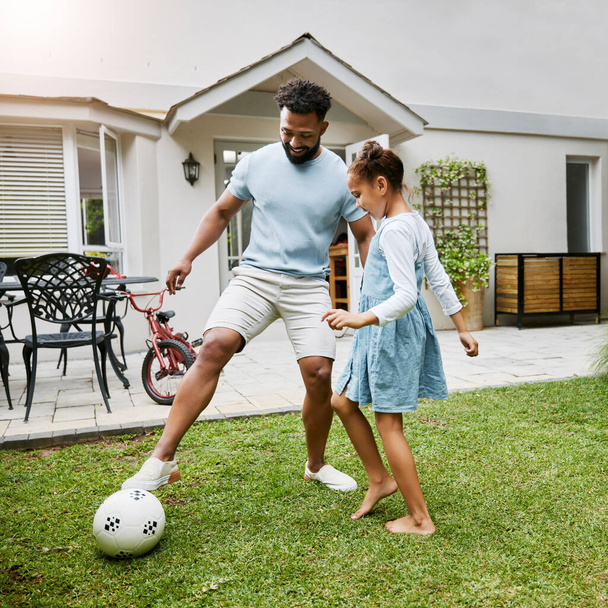 Father and daughter bonding, playing with soccer ball in backyard at home, smiling and having fun. Happy parent being playful and enjoying family time with his child. Guy being active with his kid. - Foto, imagen