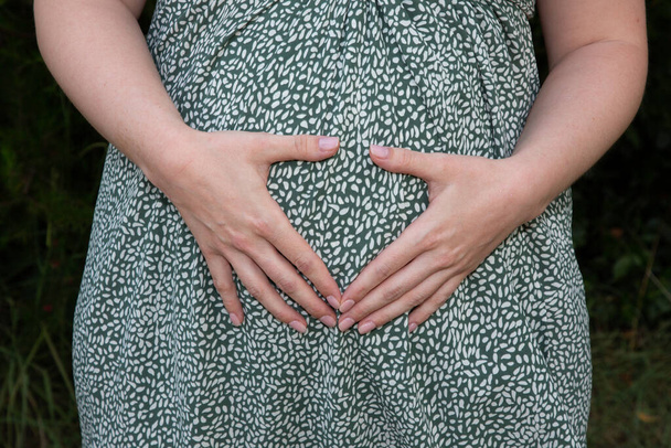 έγκυος γυναίκα χέρια κάνουν το δάχτυλο της καρδιάς στην κοιλιά - Φωτογραφία, εικόνα