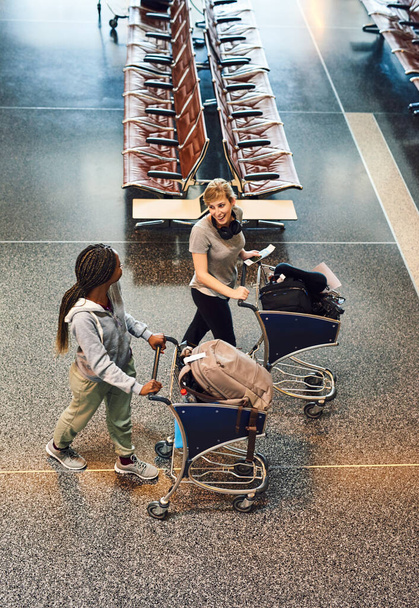 Κατευθύνεται προς το check-in αποσκευών. Υψηλής γωνίας πλάνο δύο ελκυστικών νεαρών γυναικών που περπατούν μέσα από ένα αεροδρόμιο - Φωτογραφία, εικόνα