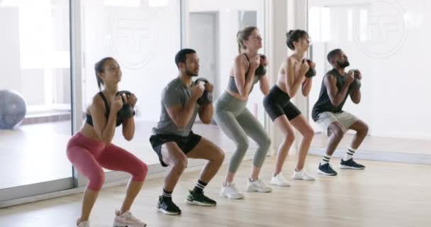 Fit, active or healthy people squatting with kettlebell weights in gym workout, exercise or training class. Diverse group of friends lifting for cardio health, stamina or endurance or building muscle. - Filmati, video