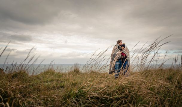 Молода пара обіймається на відкритому повітрі під ковдрою в холодний день
 - Фото, зображення