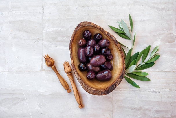 Tasty olives in wooden bowl with serving picks or forks and green branches on light background - Photo, Image